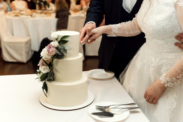 De bruid en bruidegom snijden hun rustieke bruidstaart aan tijdens het bruiloftsbanket. close-up handen die een mooie cake snijden