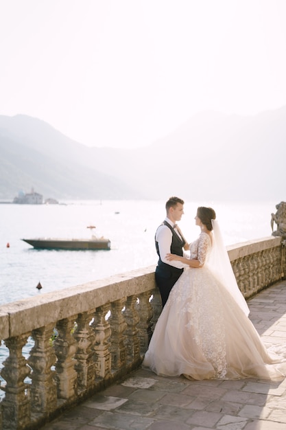 De bruid en bruidegom staan op een groot terras met stenen zuilen die uitkijken over de baai van Kotor