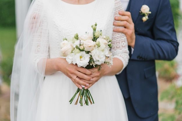 De bruid houdt in haar handen een prachtig boeket van delicate bloemen en groene bladeren