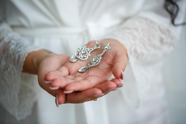 De bruid houdt oorbellen in haar hand op haar trouwdag. sieraden voor een vakantie voor de pasgetrouwden