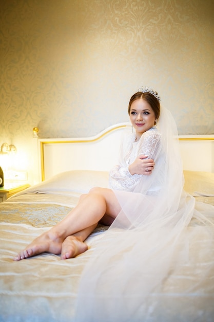 De bruid in een witte jas op het bed op een huwelijksochtend