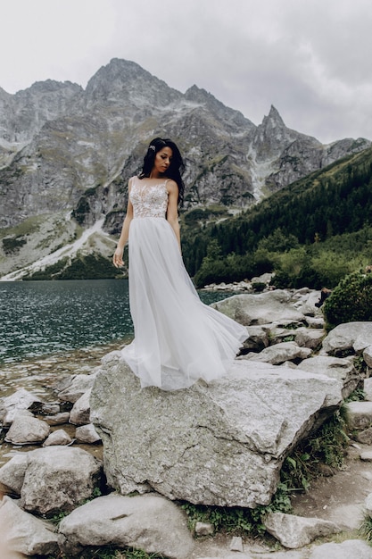 De bruid in een witte jurk en bruidegom staan in de buurt van de rivier en knuffelen en zonneschijn