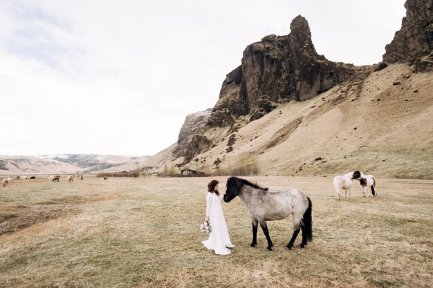 De bruid in een witte jurk en een boeket in haar handen streelt een paard met zwarte manen in het gezicht