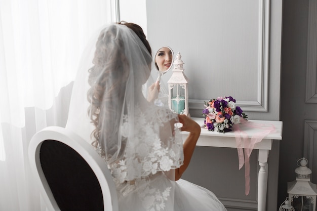De bruid kijkt naar zichzelf in een spiegel in de slaapkamer.