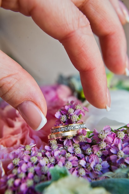 De bruid neemt de hand van gouden trouwringen met diamanten.