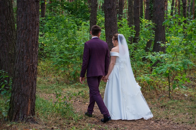 de bruidegom en de bruid lopen in trouwjurken door het bos