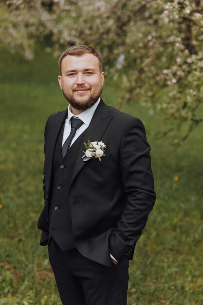 De bruidegom gekleed in een zwart pak loopt vooruit op groen gras in de natuur Een elegante man in een klassiek zwart pak Portret van een man