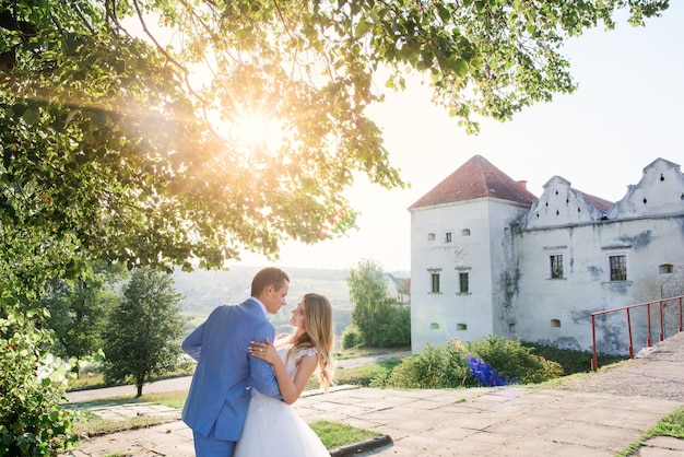 De bruidegom houdt bruid het tedere stellen met haar vóór een oud kasteel in een zonnige de zomerdag