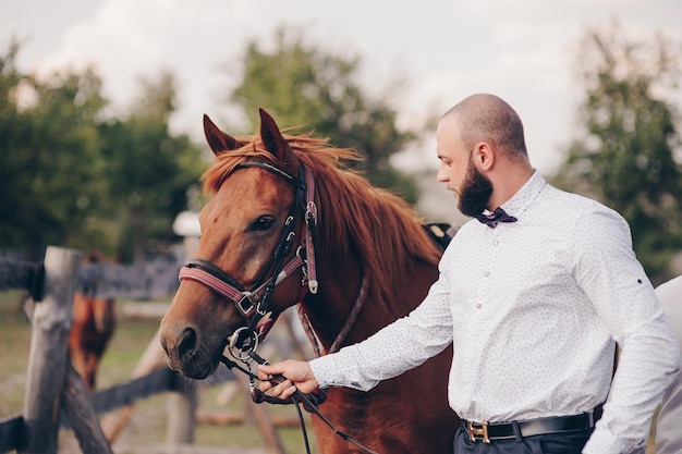 Foto de bruidegom in een wit overhemd en een paarse vlinderdas. paardrijden.