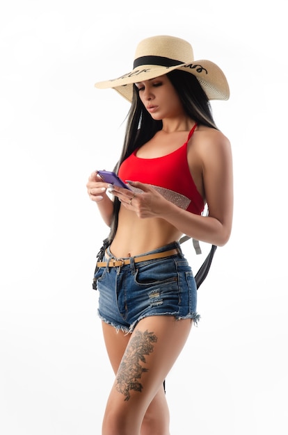 De brunette in een hoed in zomerkleren slank en sexy met een telefoon geïsoleerd op een witte achtergrond