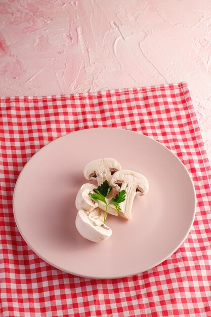 De champignon schiet gezond voedsel in roze plaat als paddestoelen uit de grond met peterseliegroen op rood tafelkleed op roze geweven achtergrond, hoekmening
