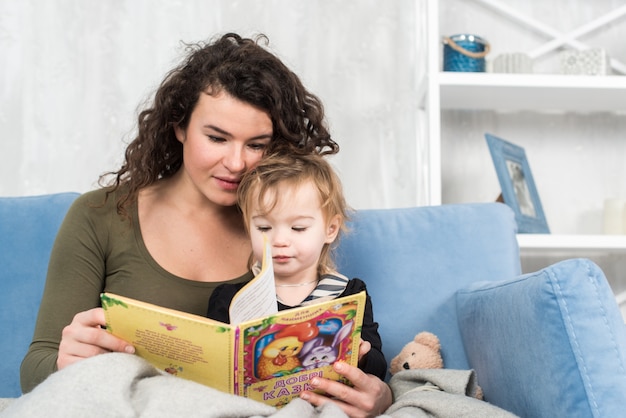 De charmante moeder toont thuis beelden in een boek aan haar schattige kleine dochter.