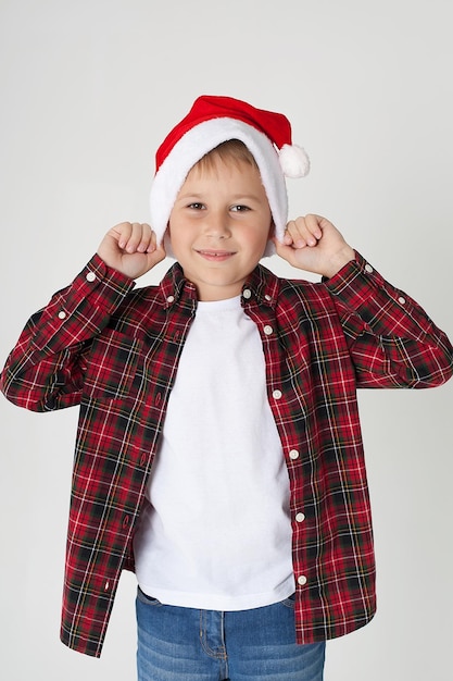 De charmante zevenjarige jongen in rode kerstmuts glimlacht met gestrekte handen omhoog De foto is gemaakt door geïsoleerd