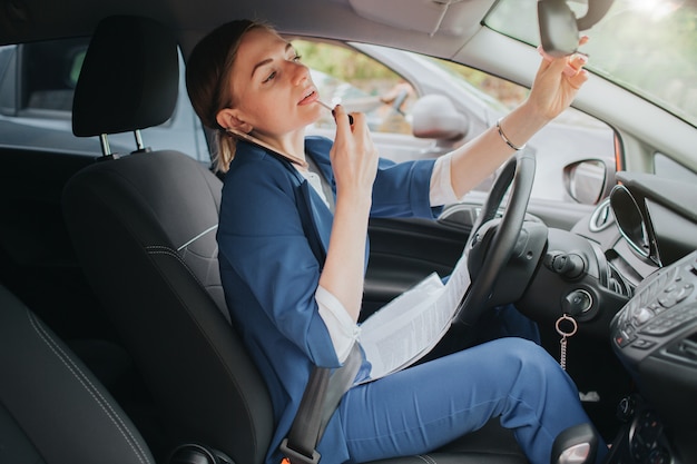 De chauffeur gaat op pad, telefoneert, werkt met documenten en maakt tegelijkertijd make-up. Zakenvrouw meerdere taken uitvoeren. Multitasking zakenvrouw.