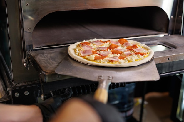 Foto de chef bereidt de pizza voor sendt de rauwe pizza in de oven