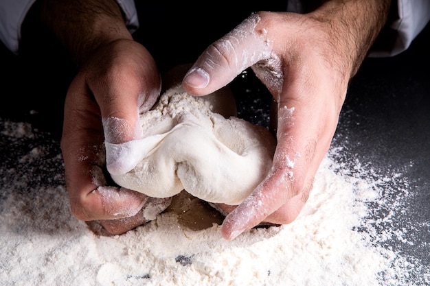 De chef kneedt het deeg op een donkere ondergrond, de tafel is bezaaid met bloem