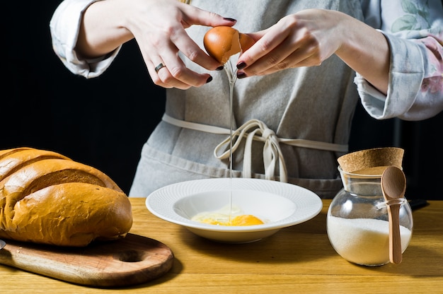 De chef-kok breekt een kippenei over een plaat. Het concept van het koken van Franse toast.