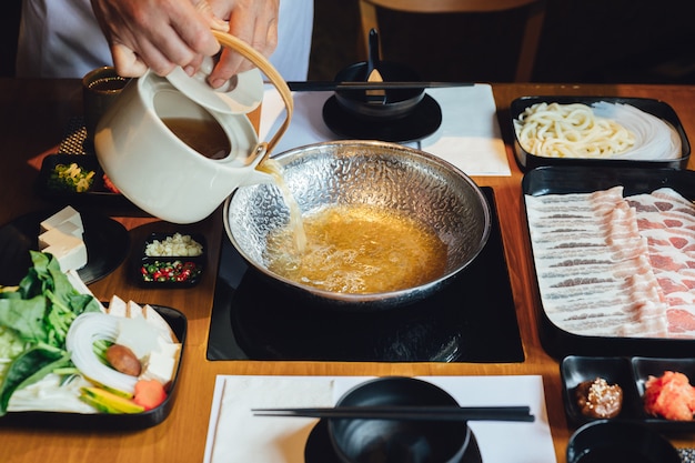 De chef-kok giet duidelijke shabu-bouillon in zilveren pot met varkensvlees kurobuta