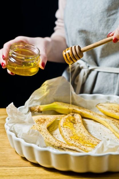 De chef-kok giet honingplakken bananen in een ovenschaal. Gebakken gefrituurde bananen.