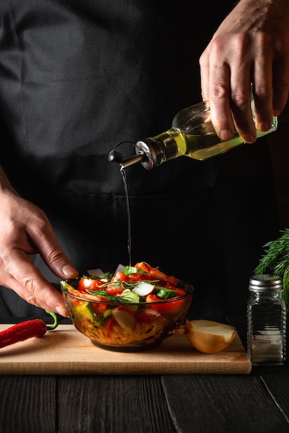 De chef-kok giet olijfolie in een kom salade. Lekker en gezond koken met een set vitamines