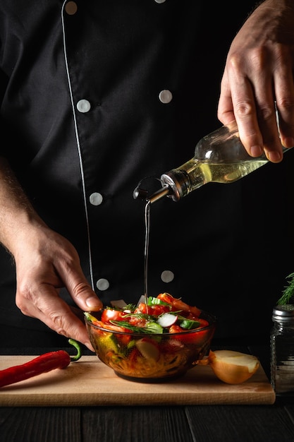 De chef-kok giet olijfolie in een kom salade. Lekker en gezond koken met een set vitamines