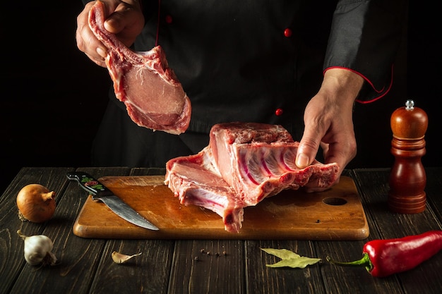 De chef-kok houdt een stuk rauw vlees met een bot in de keuken