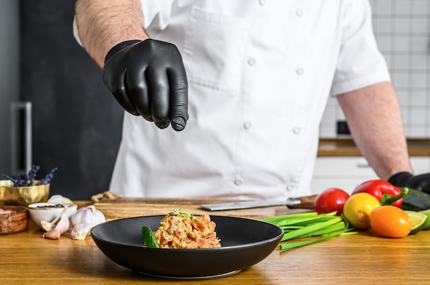 De chef-kok in zwarte handschoenen bereidt tartaar van verse tonijn