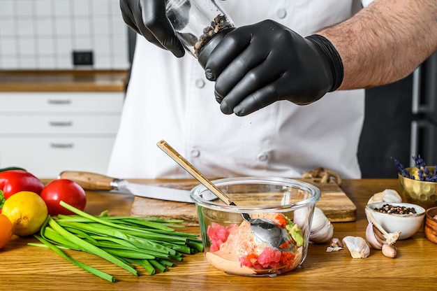 De chef-kok in zwarte handschoenen maakt tartaar van verse tonijn.