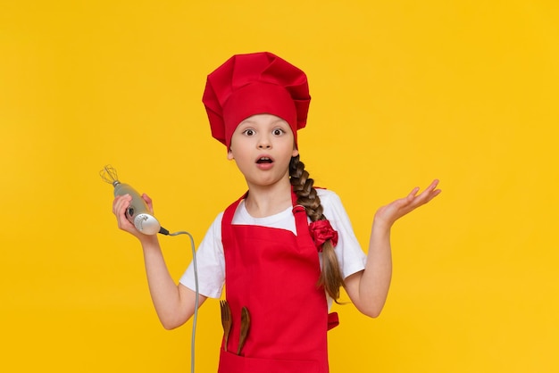 De chef-kok kind heeft een blender voor zweepslagen Een attent meisje in een rode hoed en schort Koken gerechten Gele geïsoleerde achtergrond