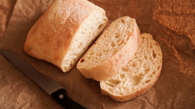 De chef-kok snijdt de ciabatta met een mes. ciabatta-plakjes op ambachtelijk papier. verse heerlijke gebakjes. vers zelfgebakken brood. gezond eten