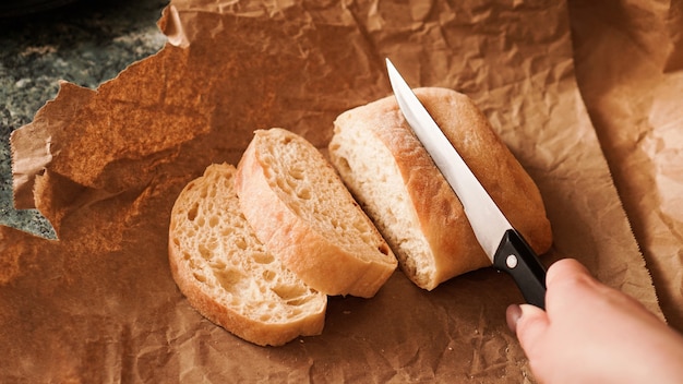 De chef-kok snijdt de ciabatta met een mes ciabatta-plakjes op ambachtelijk papier