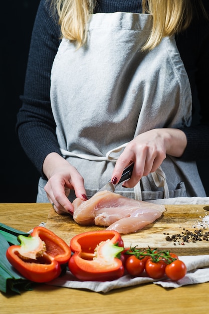 Foto de chef-kok snijdt kippenborsten op een houten snijplank.