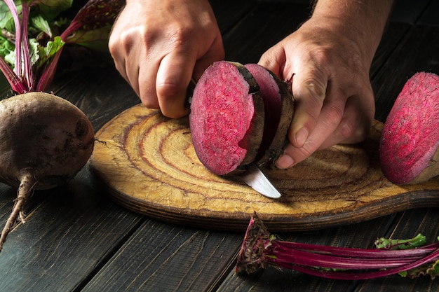 De chef-kok snijdt rode biet of beta vulgaris met een mes om heerlijke borsjt Oekraïense nationale keuken te bereiden