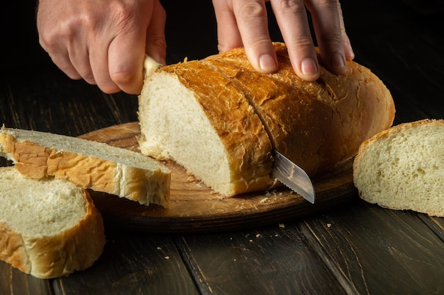 De chef-kok snijdt vers brood met een mes op een snijplank in de keuken