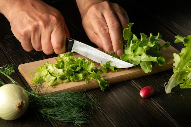 De chef-kok snijdt verse slablaadjes op een snijplank voor een vitaminesalade dieetmenu voor het ontbijt