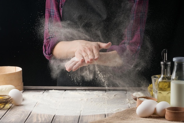 Foto de chef-kok strooit de bloem op het oppervlak zwarte achtergrond