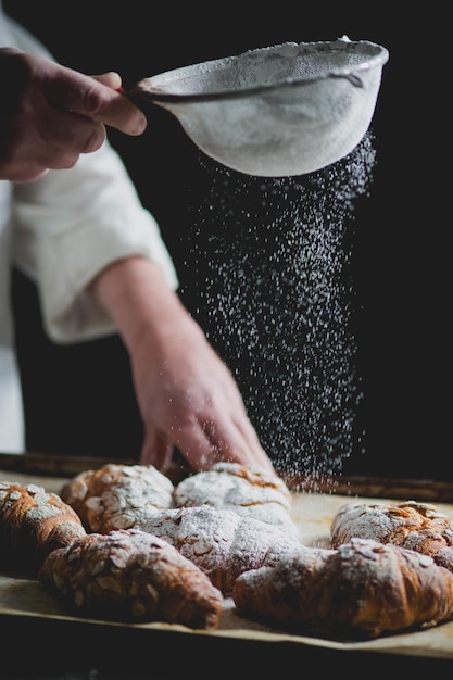 De chef-kok strooit suikerpoeder over croissants in de bakkerij.