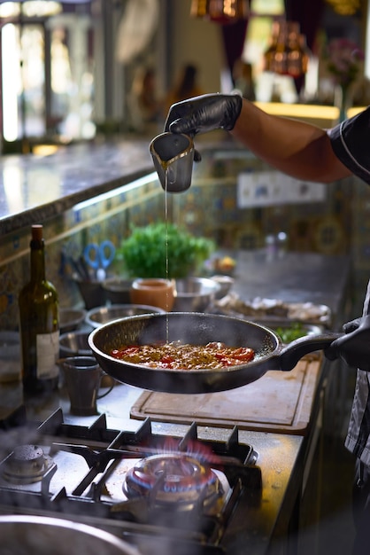 De chef-kok voegt kruiden toe, bak in een pan de tomaten en oesters het proces van het koken van spaghetti met zeevruchten