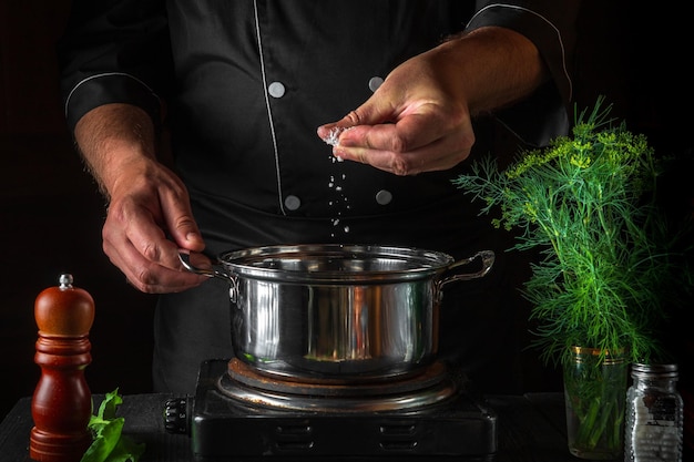 De chef-kok voegt zout toe aan de pan terwijl hij knoedels maakt Werkomgeving op vintage keukentafel