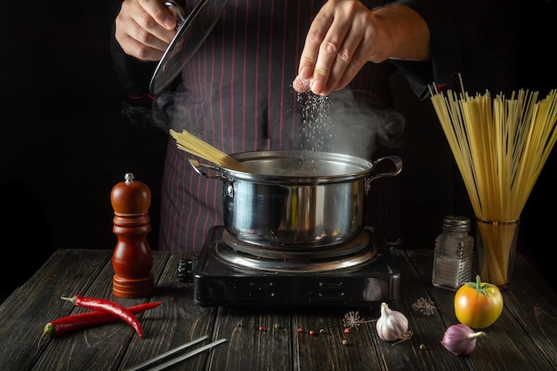 De chef-kok voegt zout toe aan een pot hete soep Koken van dieetvoeding in de keuken van een hotel of restaurant