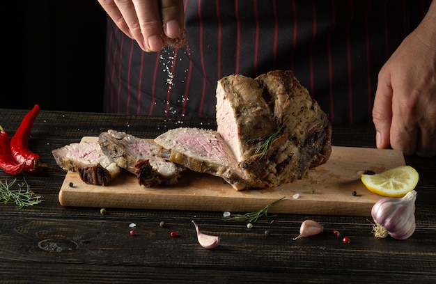 De chef-kok zout de gebakken en gesneden gemarmerde biefstuk Geserveerd op een houten plank in een rustieke stijl