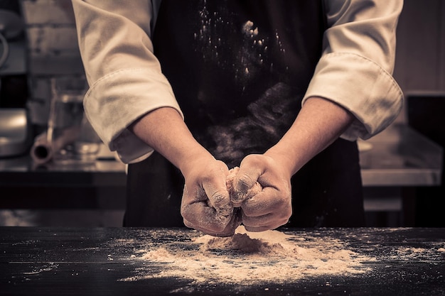 De chef maakt deeg voor pasta op een houten tafel