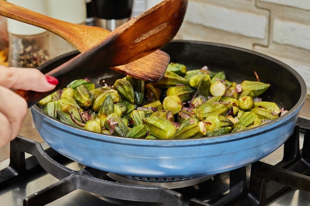 De chef roert de okra in de pan met de gebakken paarse uien