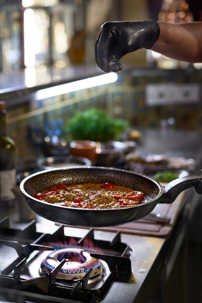 De chef voegt kruidenbak toe in een pan de tomaten en oesters, Het proces van het koken van spaghetti met zeevruchten.