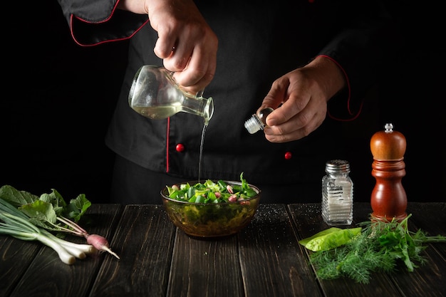 De chef voegt plantaardige olie toe aan een frisse slasalade een vegetarisch ontbijt bereiden in de keuken