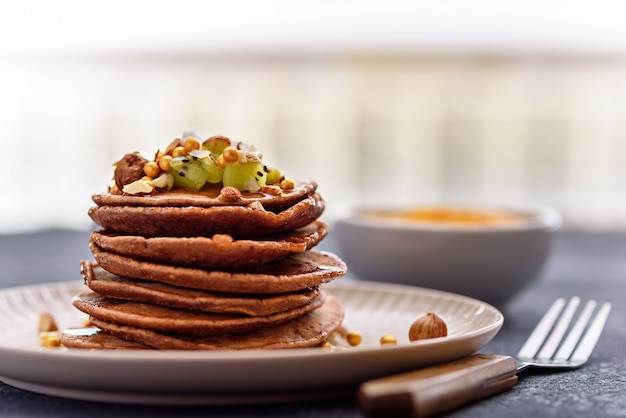 De chocoladepannekoeken van de close-upstapel met kiwi, hazelnoot, ahornsiroop op plaat met vork op keukentafel