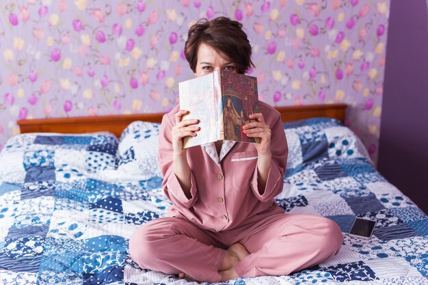 De close-up van de vrouw draagt pyjama en ontspant thuis en leest een boek. Blijf thuis. Quarantaine
