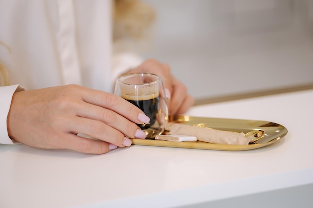 De close-up van de vrouw neemt een kopje koffie tijdens het wachten op de cosmetische procedure transparant glas met