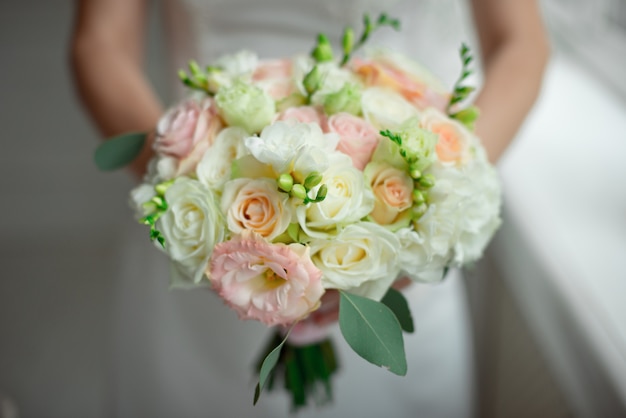 De close-upbruidegom in een kostuum en de bruid in een witte kleding staan en houden een boeket van perzikrozen