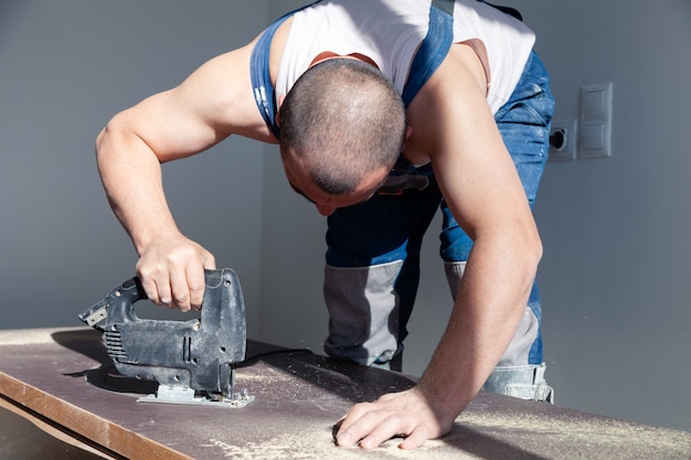 De close-uphand van timmerman, schrijnwerker met professionele snijgereedschapzaag of figuurzaag, sneed houten tafelblad, zaagende plank, het bruine indienen, zaagsel. timmerwerkplaats, handarbeid